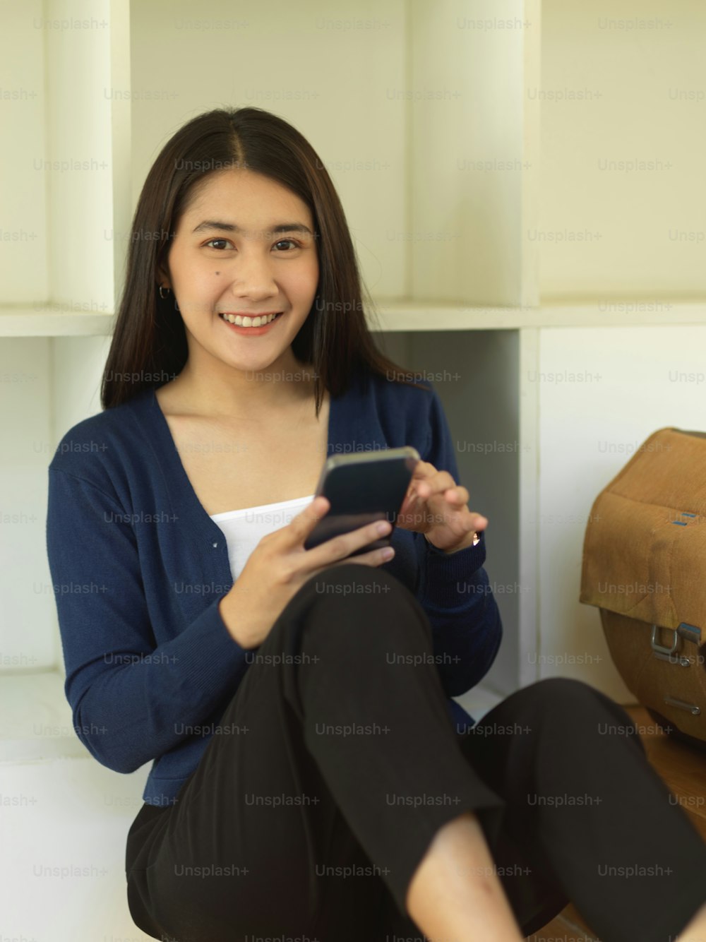 Portrait of young female teenager smiling to camera while using smartphone in living room