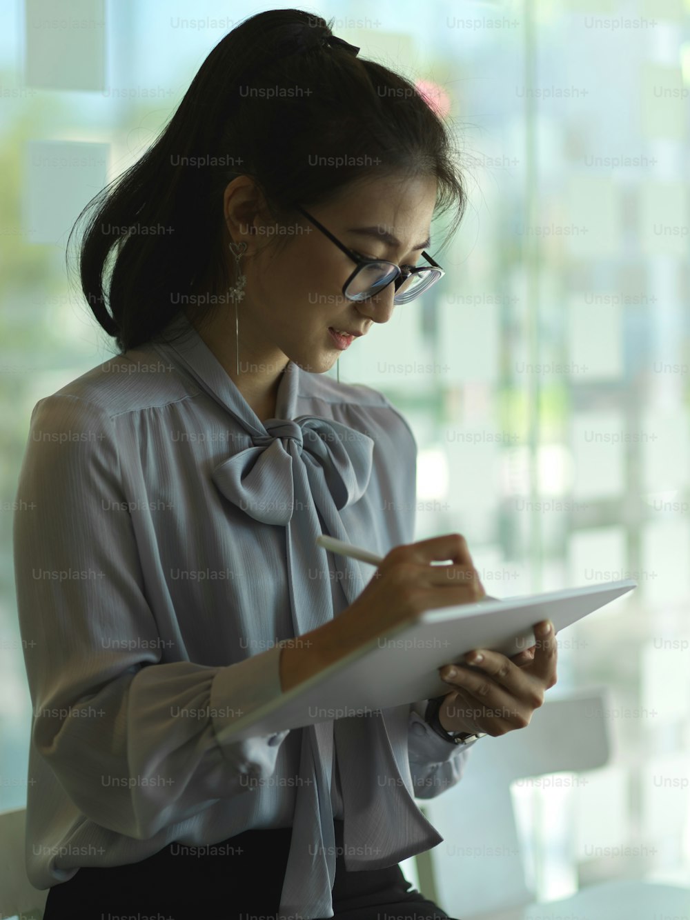 Cropped shot of businesswoman working with digital tablet while standing in glass partition office room