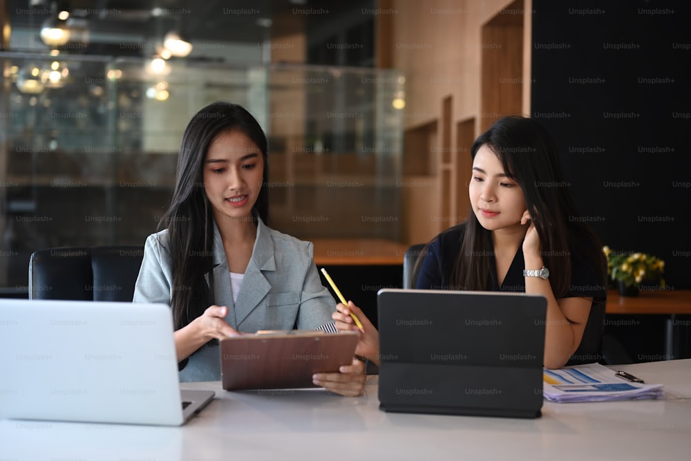 Due donne d'affari che consultano i dati sulla tavoletta digitale mentre sono sedute insieme in un ufficio moderno.