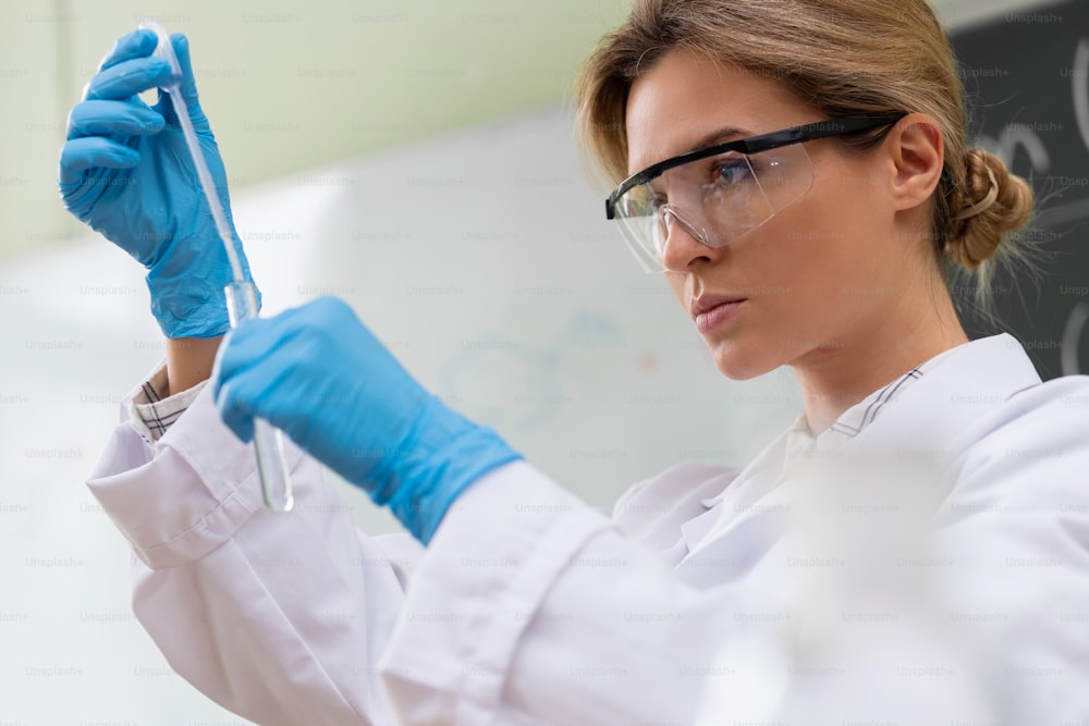 Un scientifique utilise un compte-gouttes et un tube à essai dans un laboratoire pendant des travaux de recherche.