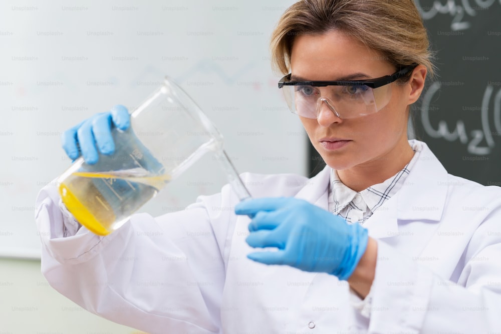 Un scientifique verse une substance du bécher à l’éprouvette dans un laboratoire pendant des travaux de recherche.