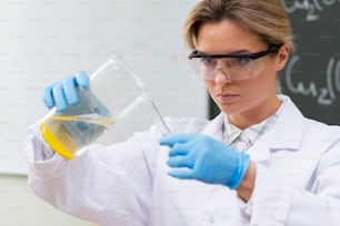 Scienziato che versa la sostanza dal becher alla provetta in un laboratorio durante il lavoro di ricerca.
