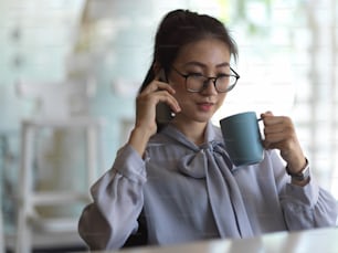 Portrait of businesswoman talking on the phone and drinking coffee while relaxing in office room