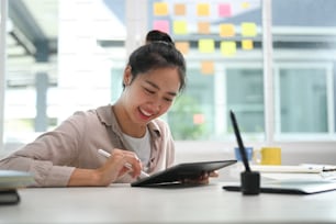 Happy designer working on digital tablet at her desk in creative office.