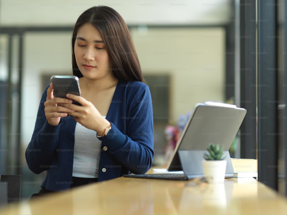 Porträt einer Studentin mit Smartphone, während sie sich von der Aufgabe im Café entspannt