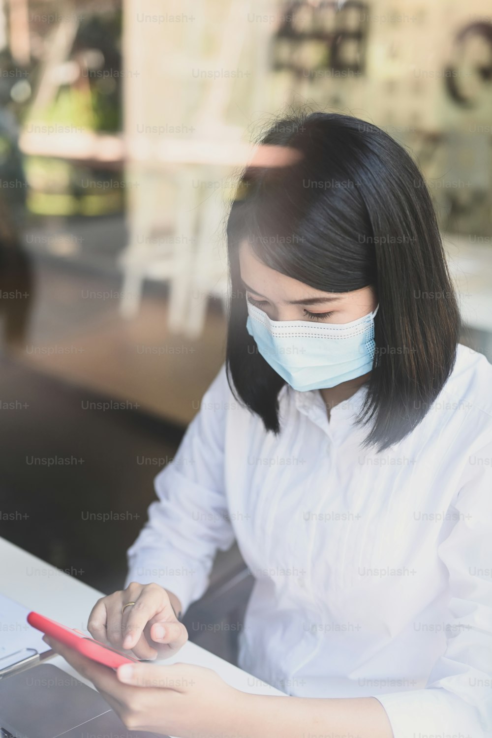 Portrait of businesswoman wearing protective mask sitting at her workspace and using mobile phone.