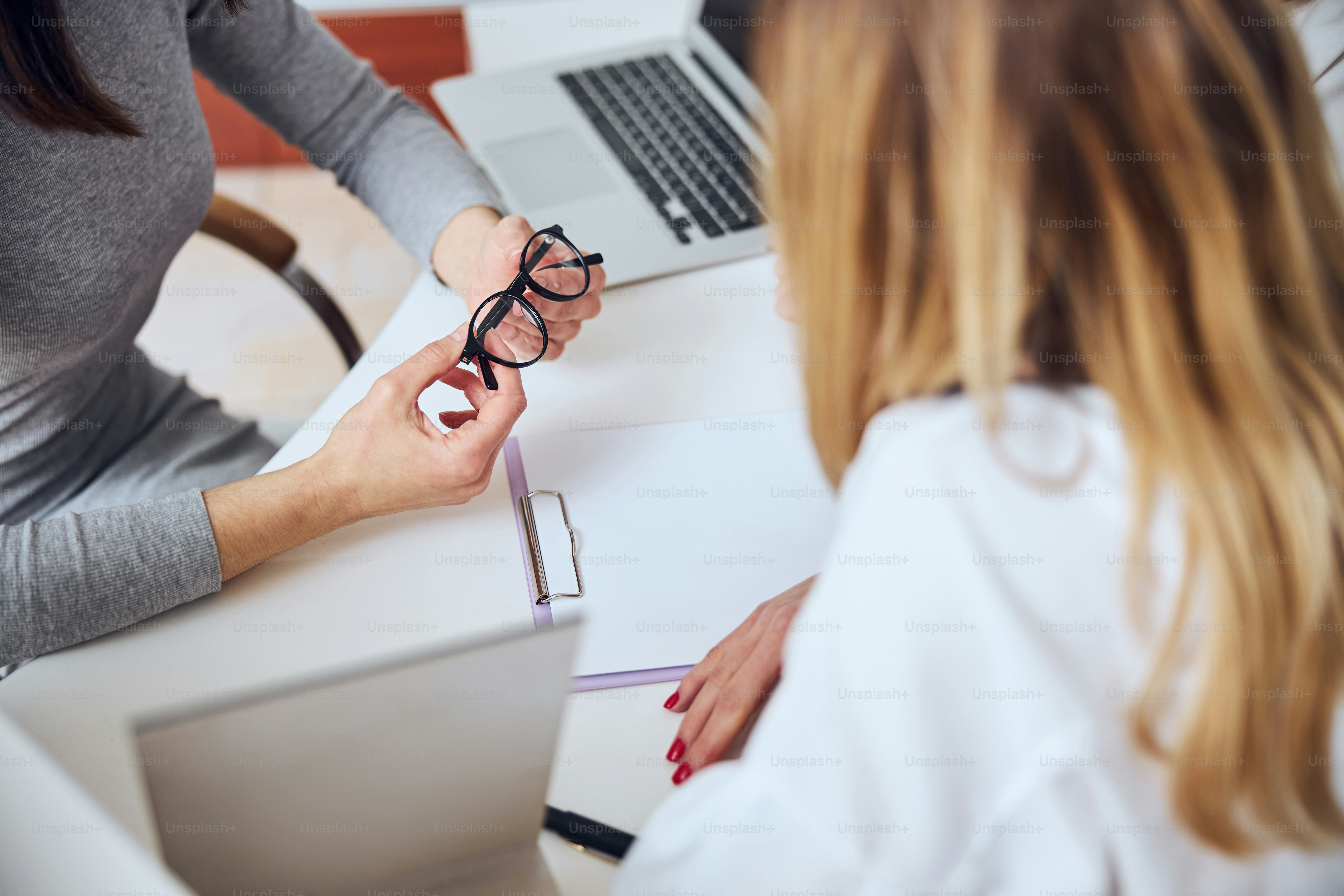 Abgeschnittenes Kopfporträt von Frauenarmen, die eine stilvolle Brille über dem Tisch im Bürooptiker halten