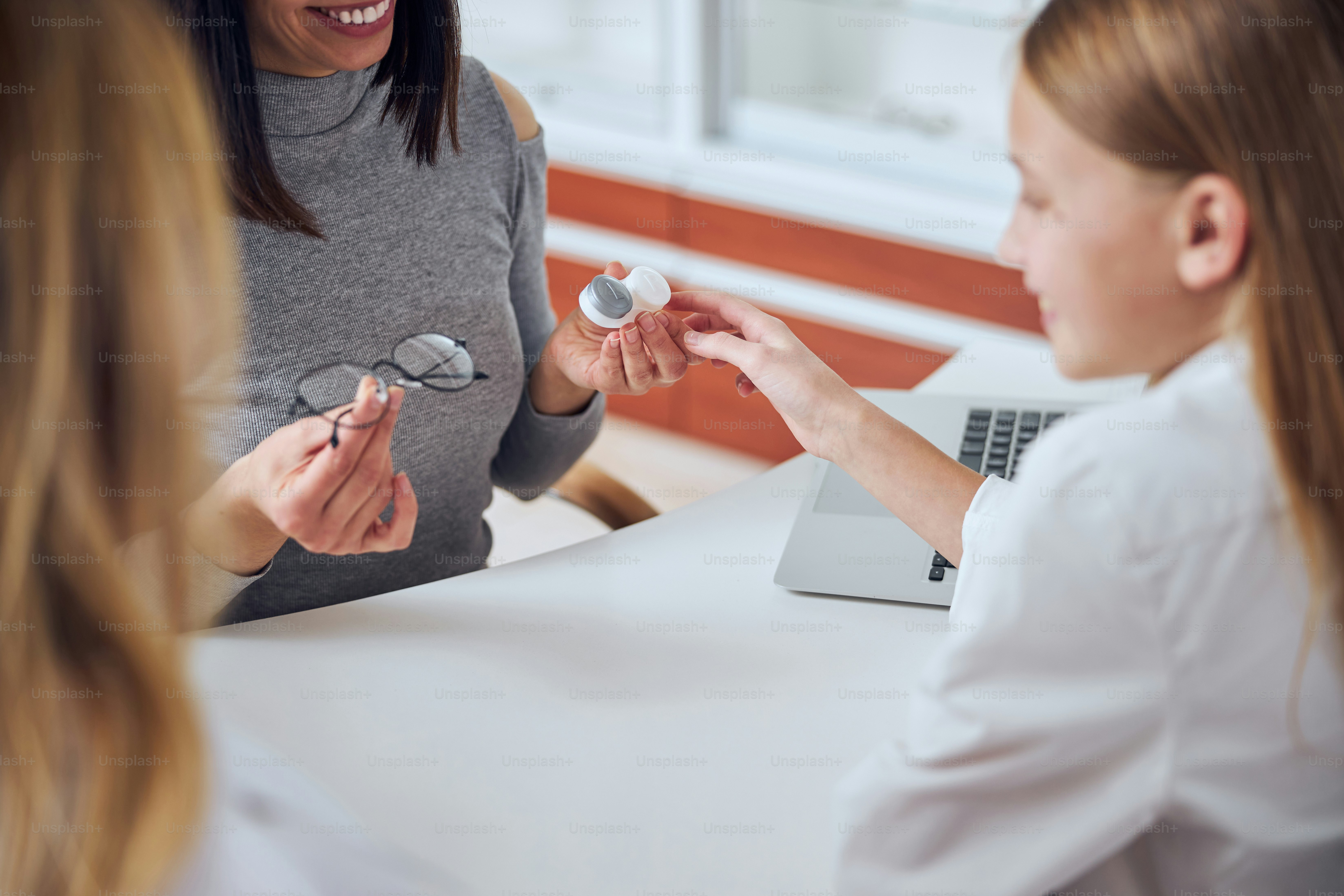 Cropped head portrait of woman in grey clothes sitting at the table while showing special tool for caring her eyes