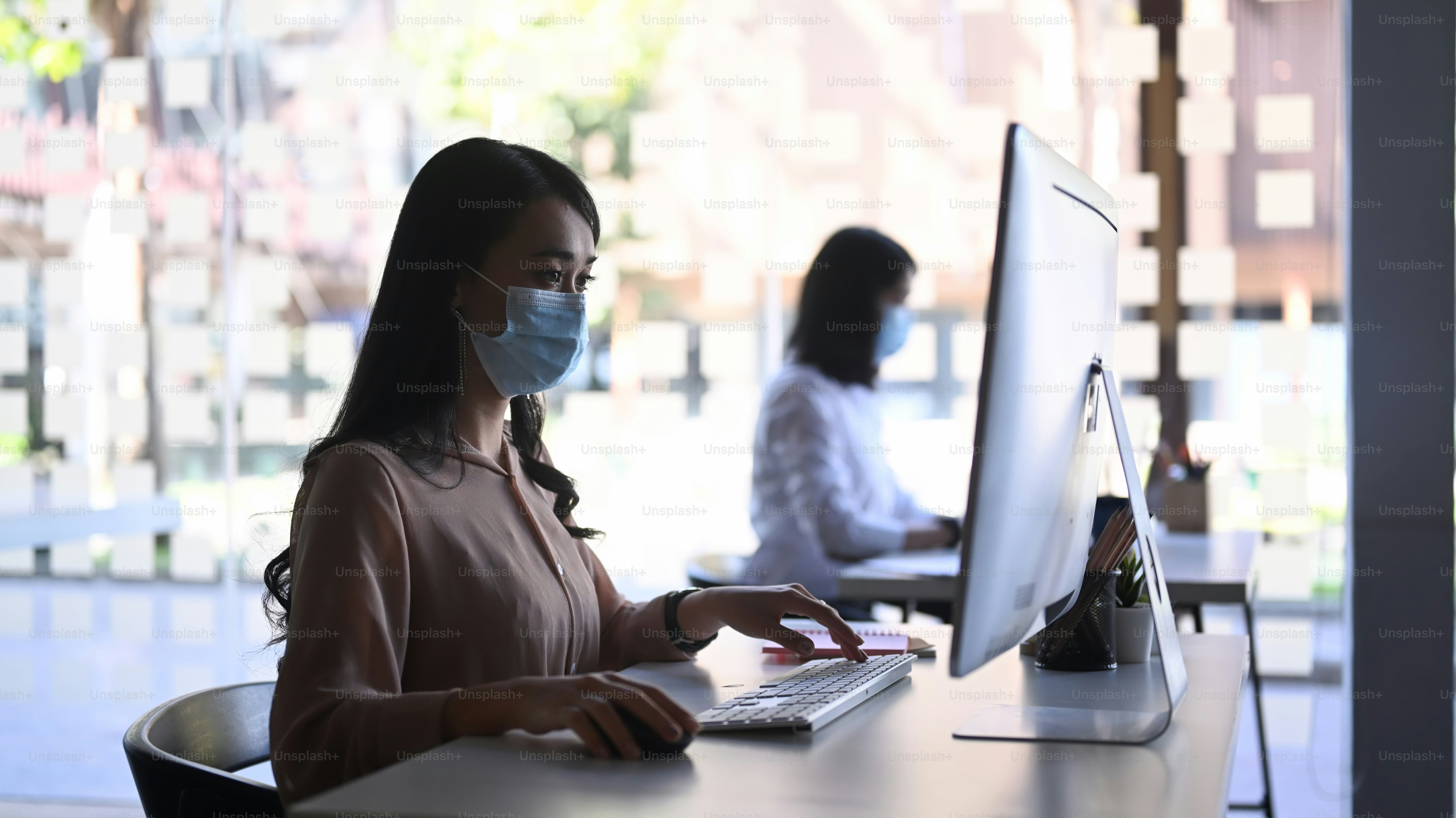 Side view of businesspeople wearing protective mask working with computer in modern office.