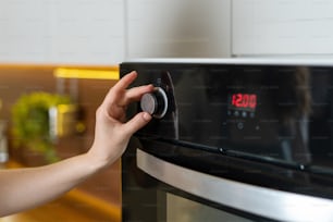 Vista ritagliata della casalinga in piedi sulla cucina moderna, regolazione della modalità di cottura sul pannello di controllo del forno elettrico, scelta della temperatura per la cottura e la cottura del cibo