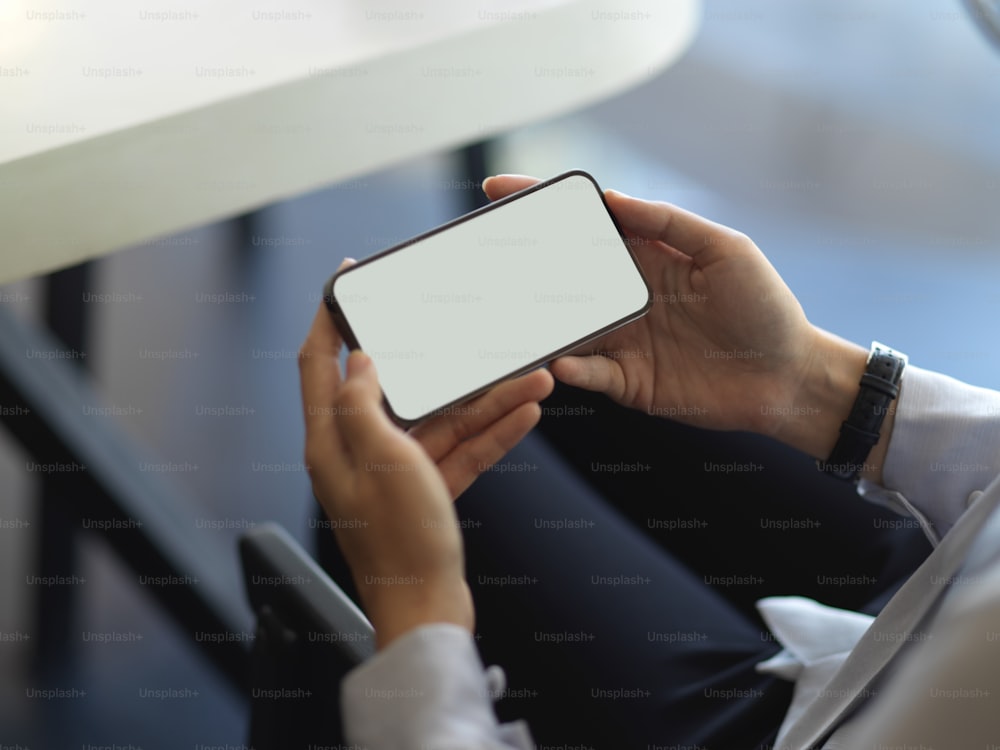 Cropped shot of female hands holding horizontal smartphone while relaxing in cafeteria, clipping path