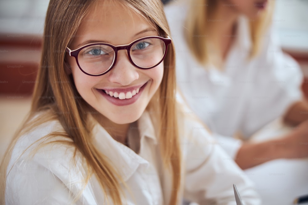 Close up portrait of happy cheerful teenager girl in glass looking and posing at the photo camera in room indoors