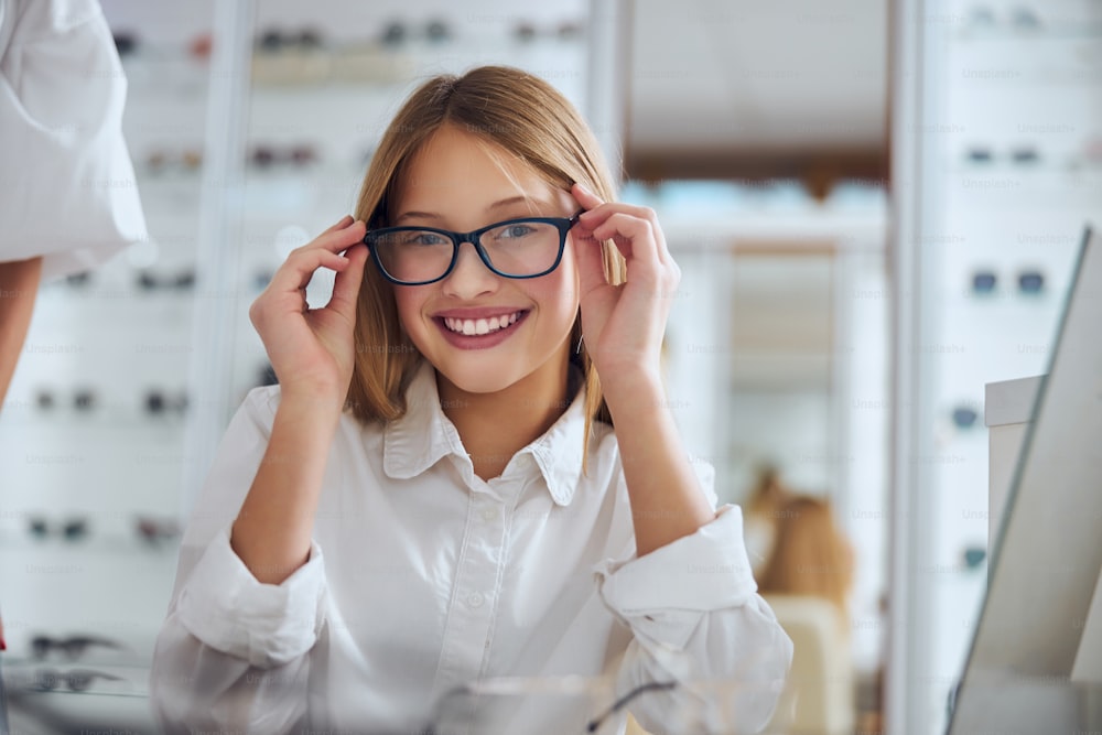 Retrato de cerca de una niña feliz y alegre con anteojos mientras está sentada en el centro óptico