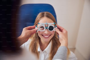 Close up portrait of good looking pretty young lady in white shirt and trial frames talking with optometrist doctor in modern ophthalmology clinic