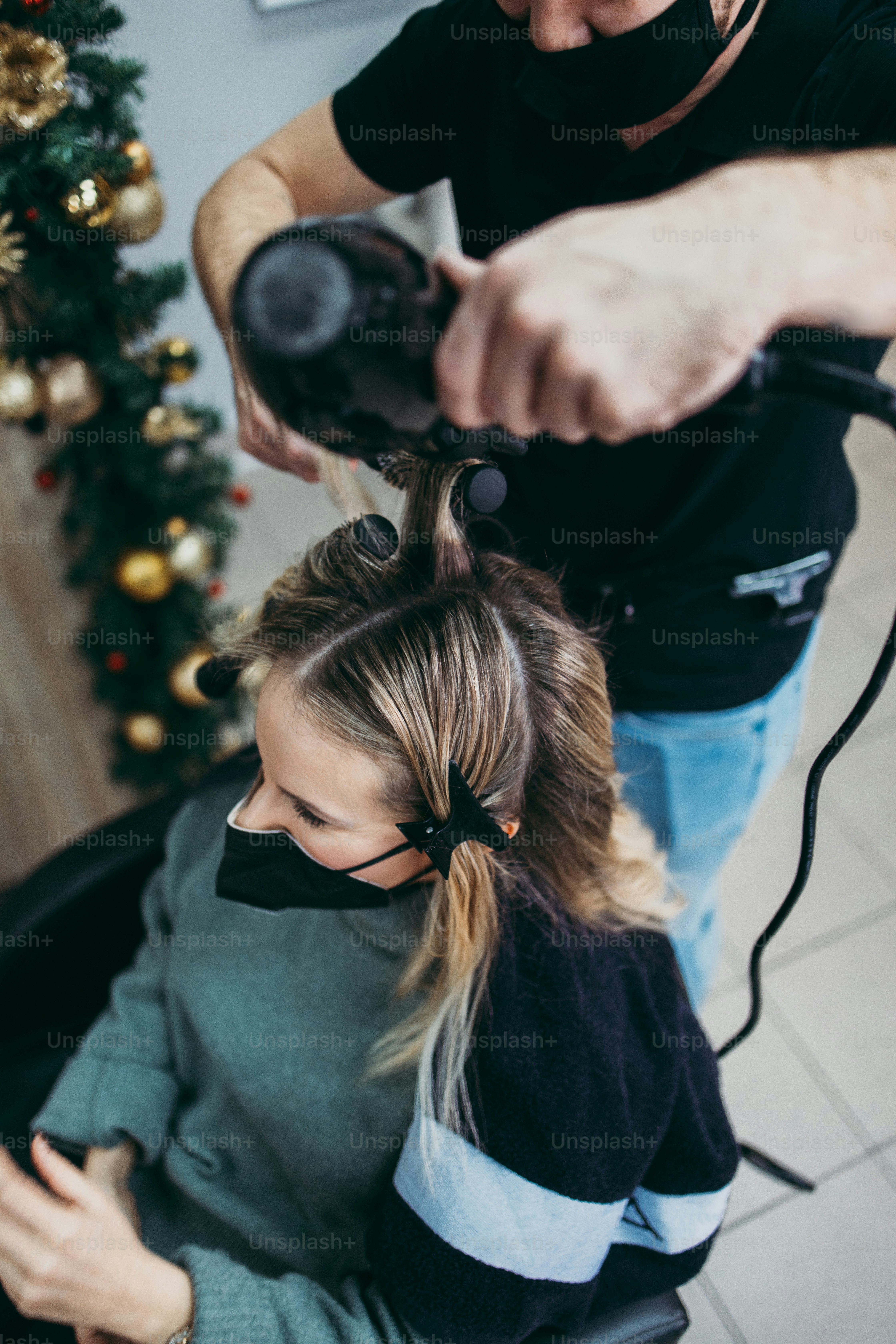 Un parrucchiere che asciuga i capelli di una donna in un salone con un albero di Natale