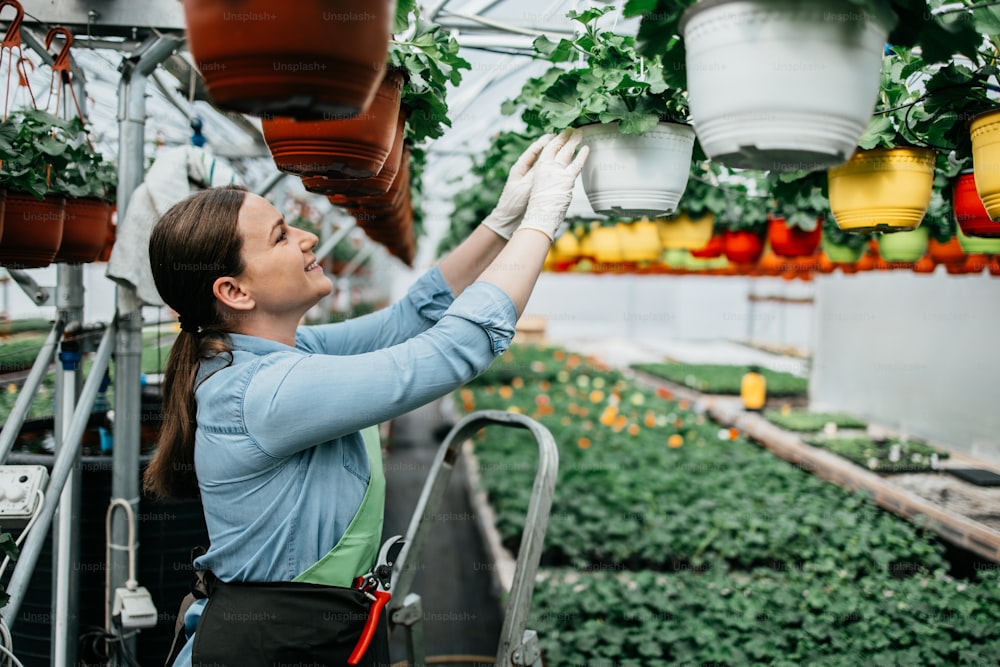 Happy and positive young adult woman working in greenhouse and enjoying in beautiful flowers.