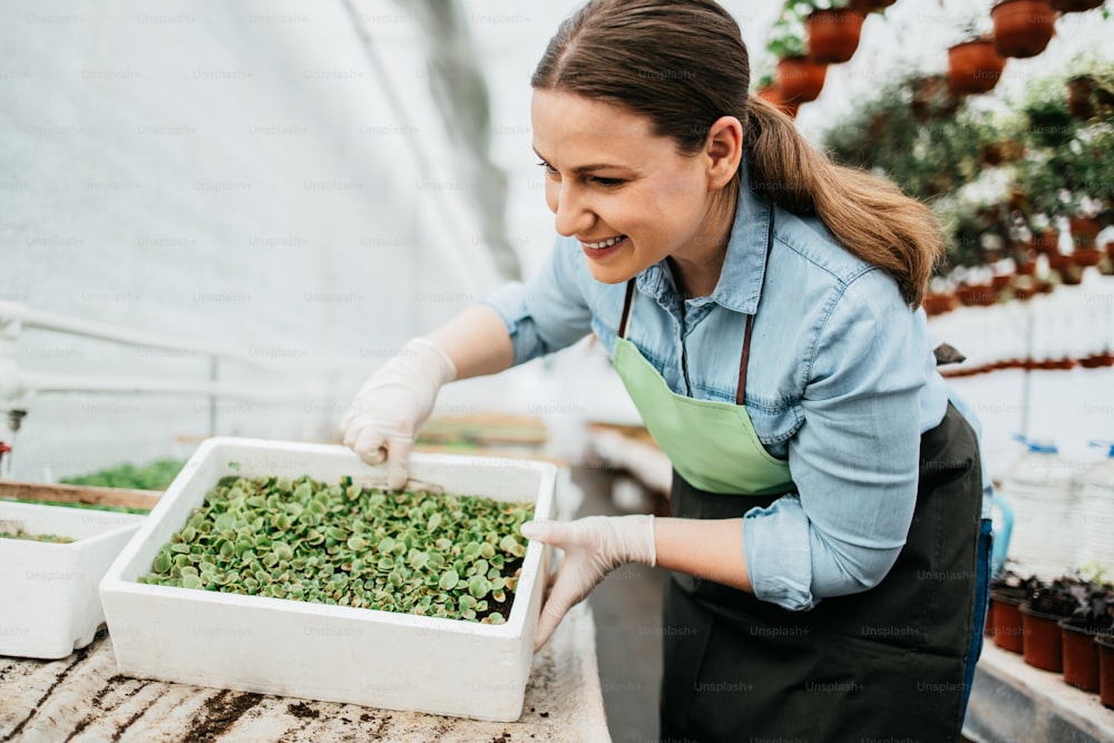 Happy and positive young adult woman working in greenhouse and enjoying in beautiful flowers.