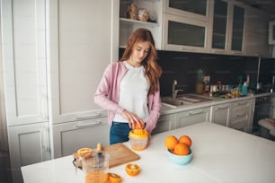 La donna caucasica dello zenzero con le lentiggini sta spremendo manualmente il succo d'arancia in cucina
