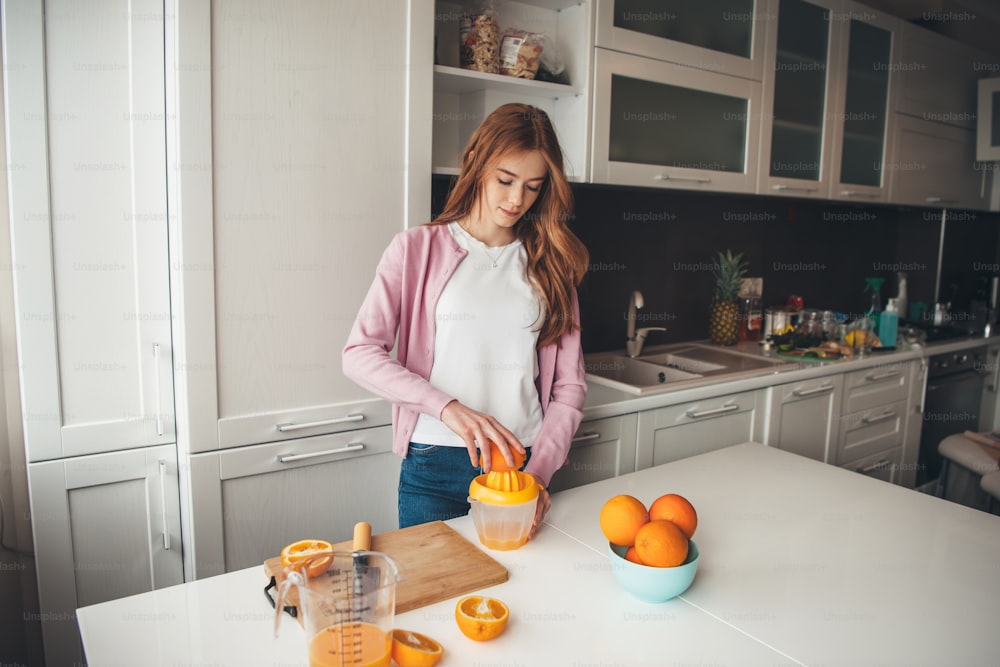 Caucasian ginger woman with freckles is manually squeezing orange juice in the kitchen