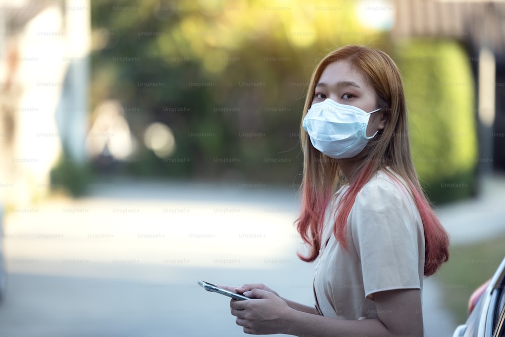 Mulher da Ásia usando uma máscara médica e usando um telefone ao ar livre