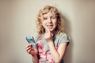 白人のブロンドの女の子は、口の中で彼女の欠けた歯を示し、歯の妖精からお金を保持しています。歯を失った自慢の子供。成長期と思春期。