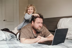 Arbeiten Sie von zu Hause aus mit Kindern. Vater arbeitet am Laptop im Schlafzimmer mit Kind Tochter auf dem Rücken. Lustiger offener Familienmoment. Neue Normalität während des Coronavirus-Quarantäne-Lockdowns.