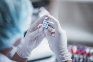 COVID-19との戦い、病院の実験室でのコロナウイルスワクチンの研究、プロの科学者がウイルス治療注射用の新しいワクチンのボトルを持ち、パンデミック時の医学臨床