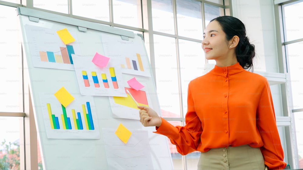 Jovem explica dados de negócios em quadro branco em sala de escritório casual. A confiante empresária asiática relata o progresso das informações de um projeto de negócios para se associar para determinar a estratégia de mercado.
