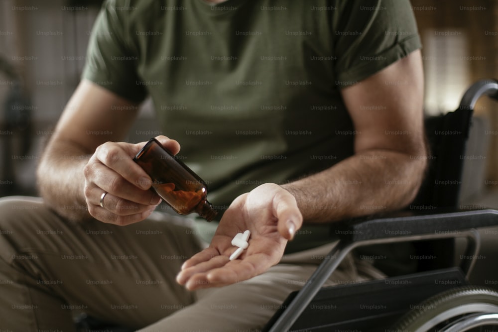 Triste e infeliz homem deprimido em cadeira de rodas está segurando uma pílula em uma mão. Close up do homem segurando punhado de pílulas.