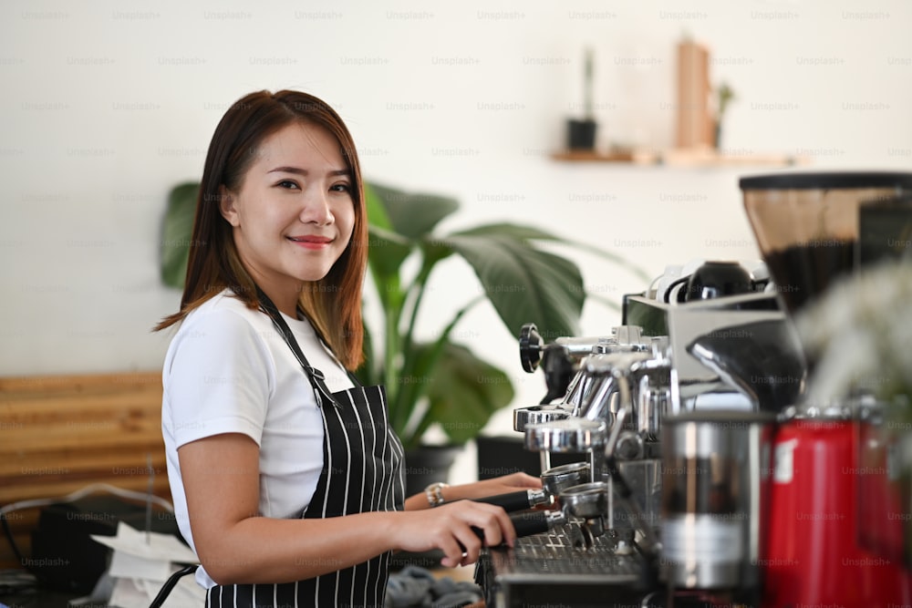 Female Asian Barista preparing cup of coffee for customer order in coffee shop.