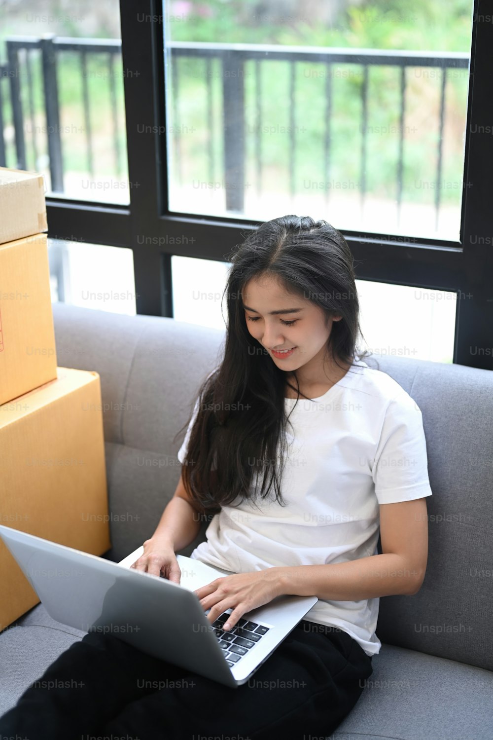 若いアジアのビジネスは、ソファに座ってウェブサイトから顧客の注文をチェックするためにラップトップを使用してオンライン販売者の所有者を開始します。