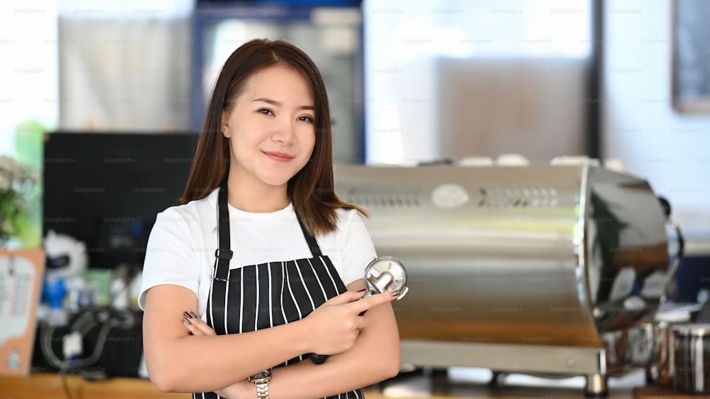 喫茶店のカウンターで腕を組んで立っている若い女性起業家の横長写真。