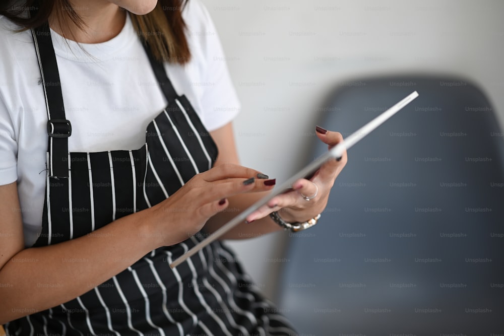 Ausschnittaufnahme der Cafébesitzerin, die in ihrem Café sitzt und ein digitales Tablet benutzt.