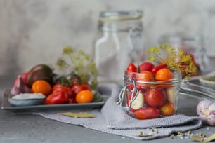 Konservierung von frischen und eingelegten Tomaten, Gewürzen und Knoblauch auf einem grauen Betontisch. Gesunde fermentierte Lebensmittel. Hausgemüse in Dosen.