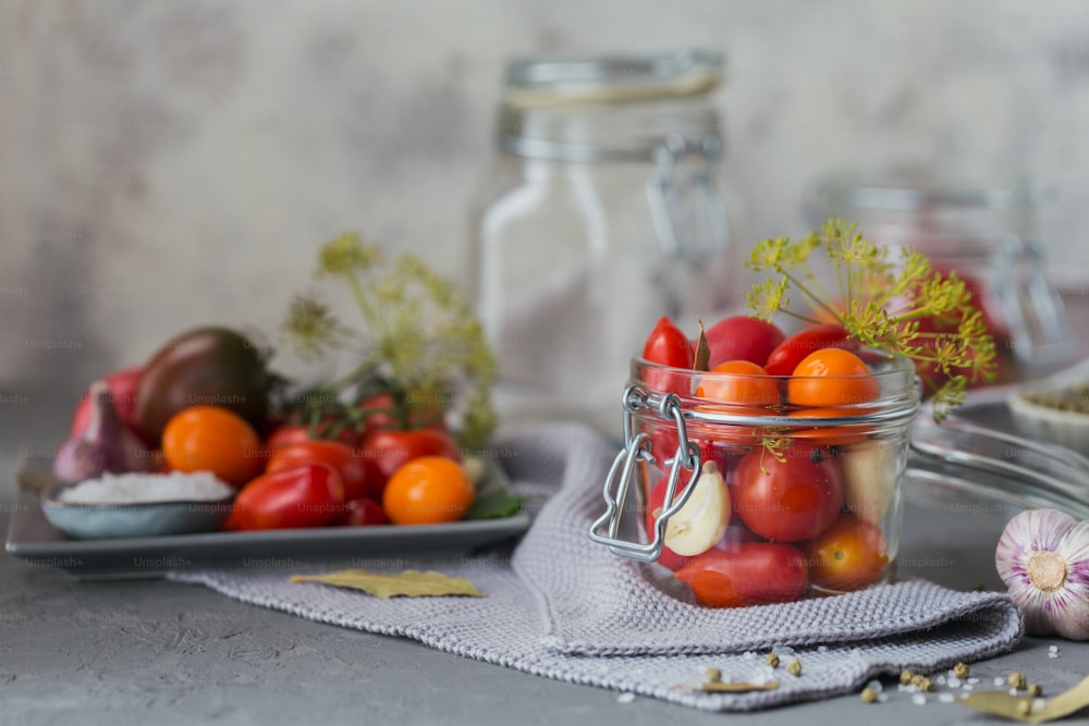 Preserving fresh and pickled tomatoes, seasonings and garlic on a grey concrete table. Healthy fermented food. Home canned vegetables.