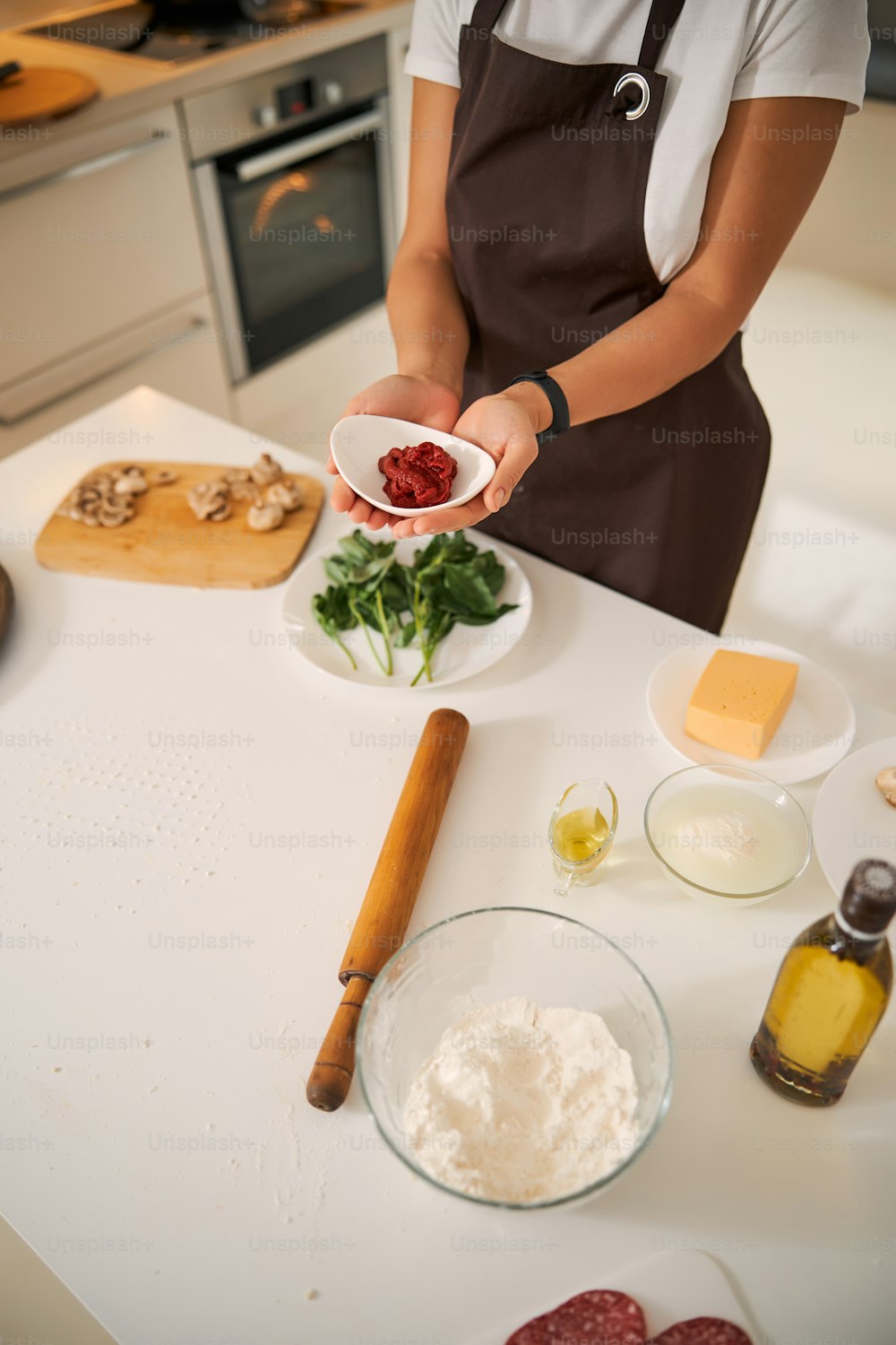 Foto recortada de una mujer sosteniendo un tazón pequeño con salsa de tomate sobre la mesa con ingredientes de pizza