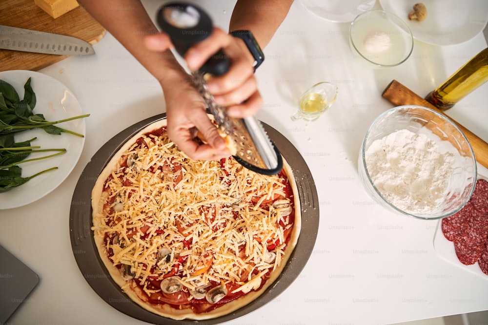 Vista superior de una pizza en una bandeja para hornear y una mujer rallando queso en la parte superior