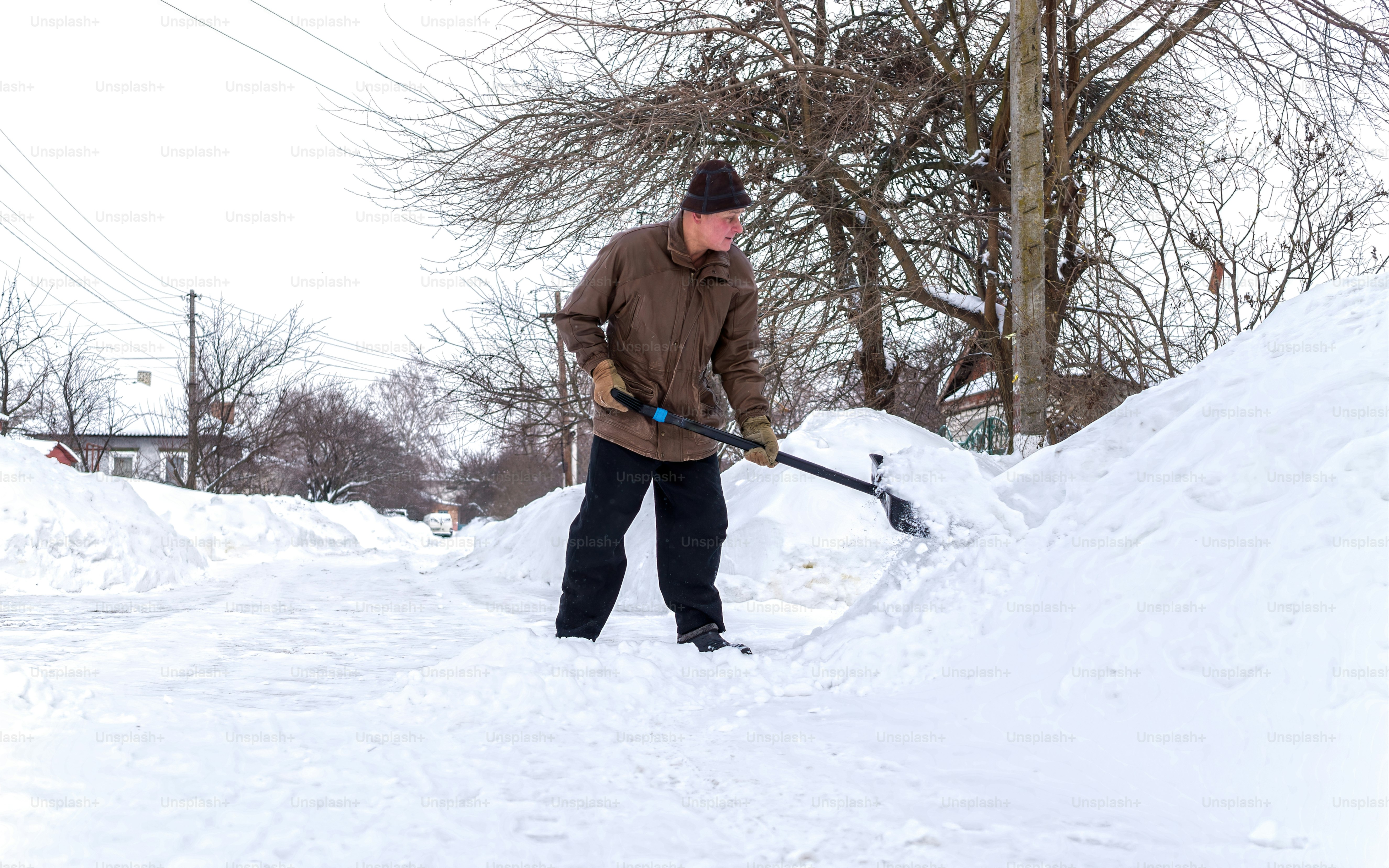 elderly man with a shovel in his hands clears the street after a heavy snowfall. Man at seasonal work