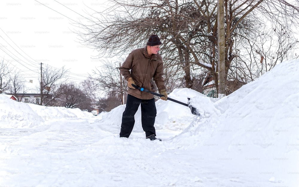 elderly man with a shovel in his hands clears the street after a heavy snowfall. Man at seasonal work