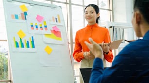 Mujer joven explica los datos de negocios en la pizarra blanca en la sala de oficina informal. La empresaria asiática segura de sí misma informa sobre el progreso de la información de un proyecto empresarial para asociarse para determinar la estrategia de mercado.