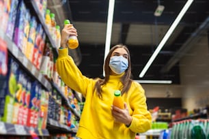 Junger Mensch mit Schutzmaske beim Einkauf von Lebensmitteln im Supermarkt. Vorbereitung auf eine pandemische Quarantäne aufgrund des Coronavirus-Covid-19-Ausbruchs. Auswahl von nicht verderblichen Lebensmittel-Essentials Stockfoto