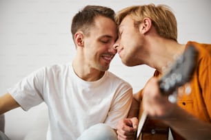Handsome young man holding guitar and sharing tender moment with boyfriend, Isolated on white background