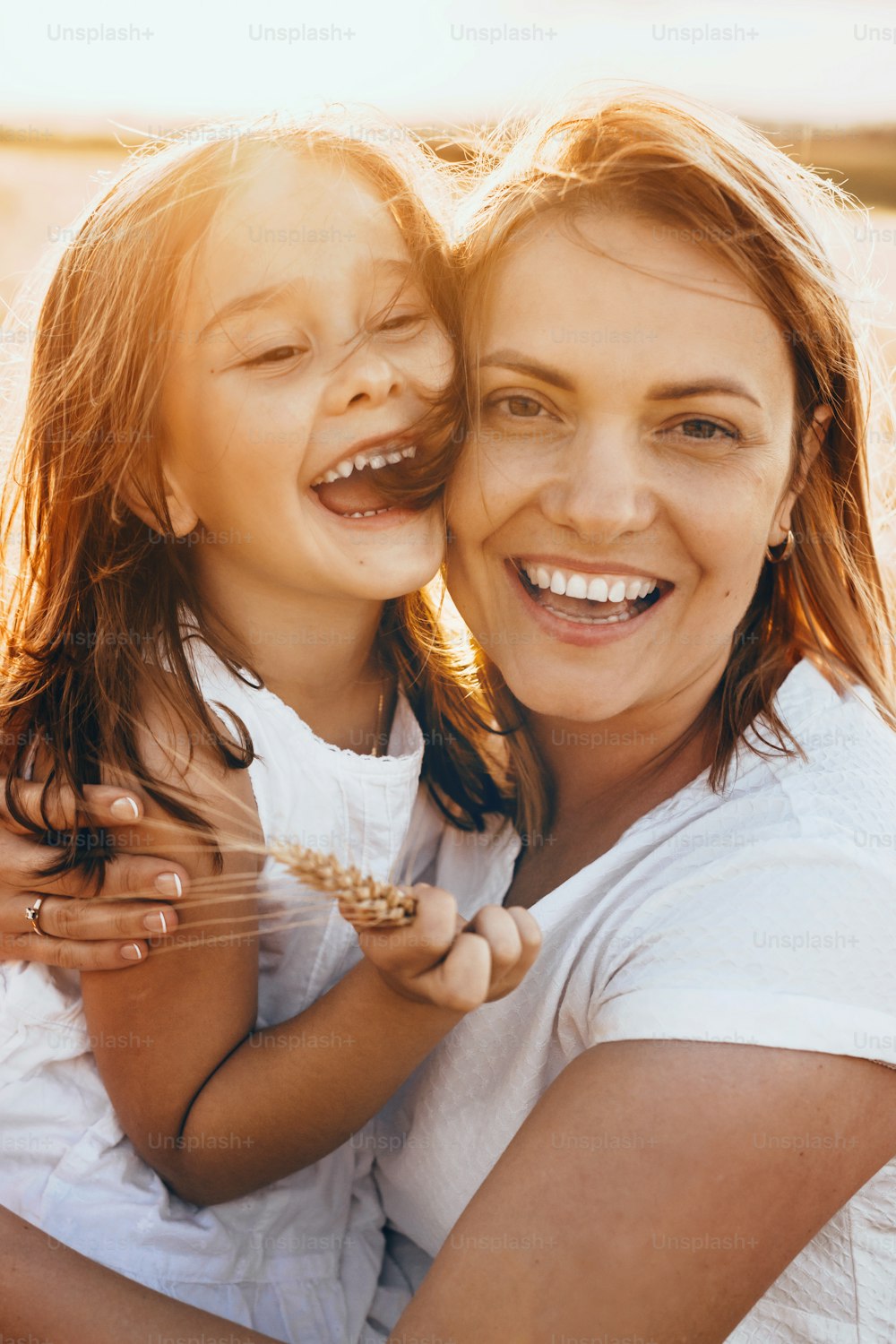 Glückliche Mutter und ihre Tochter posieren im Sonnenschein mit Weizensamen lächelnd in die Kamera