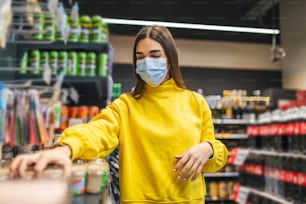 Mujer con máscara protectora y comprando alimentos en la tienda de comestibles durante la epidemia de virus. Mujer joven con una máscara protectora y guantes comprando en tiempos de pandemia de virus, comprando suministros de alimentos
