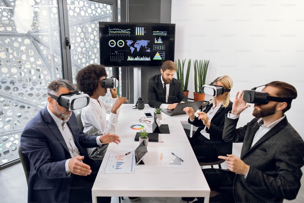 Business team working in vr glasses. Male boss working on laptop in office, while his multiethnic team works with virtual reality goggles and developing a project