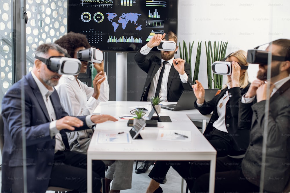 VR, business meeting conference. Multiethnical male and female business people wearing virtual reality headsets, touching air and gesturing at the office, working with new project or program.