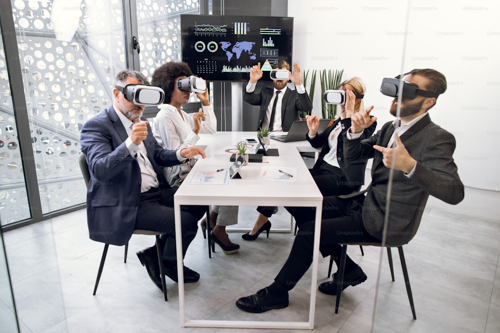 Seminario di team building, concetto di tecnologia. Uomini d'affari multirazziali, utilizzando occhiali VR, formando il team, gesticolando e divertendosi a lavorare insieme.