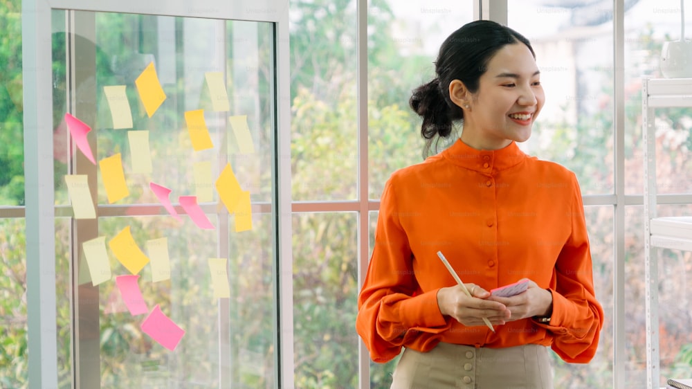 Business people work on project planning board in office and having conversation with coworker friend to analyze project development . They use sticky notes posted on glass wall to make it organized .