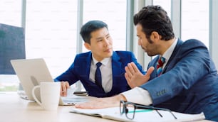 Two business people talk project strategy at office meeting room. Businessman discuss project planning with colleague at modern workplace while having conversation and advice on financial data report.