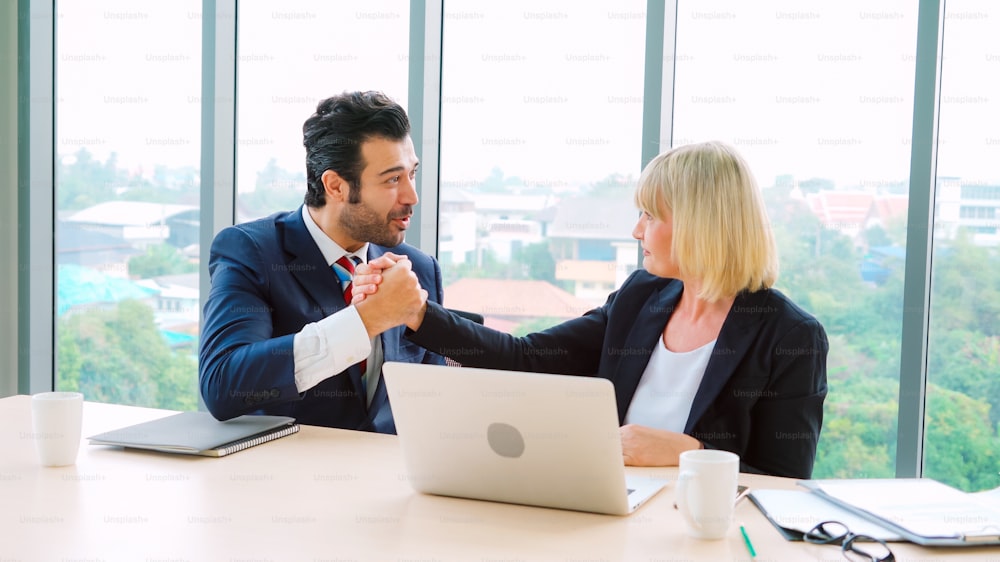 Two happy business people celebrate at office meeting room. Successful businessman congratulate project success with colleague at modern workplace while having conversation on financial data report.